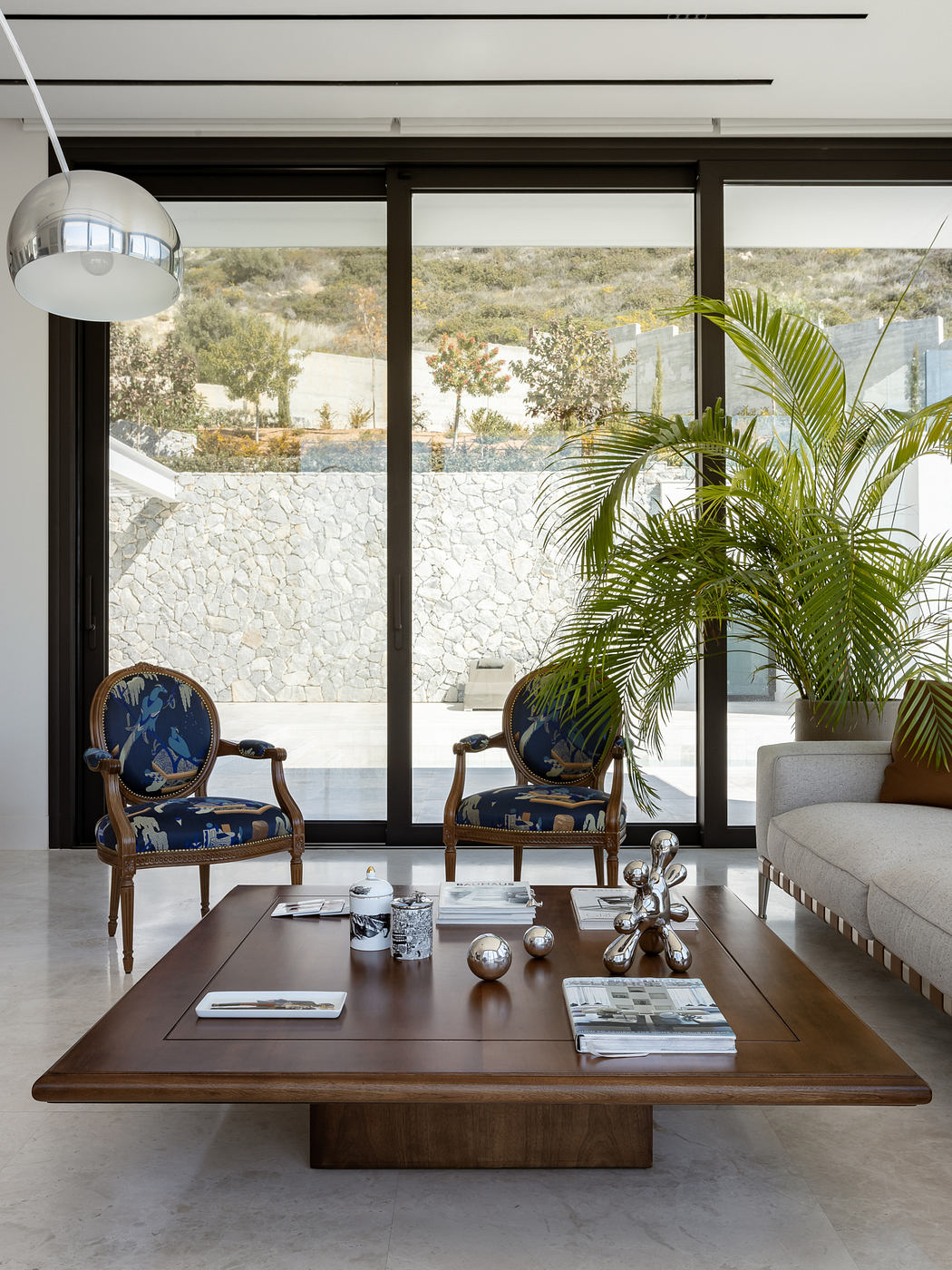 A modern, spacious living room with stone walls, large windows, and stylish furniture.