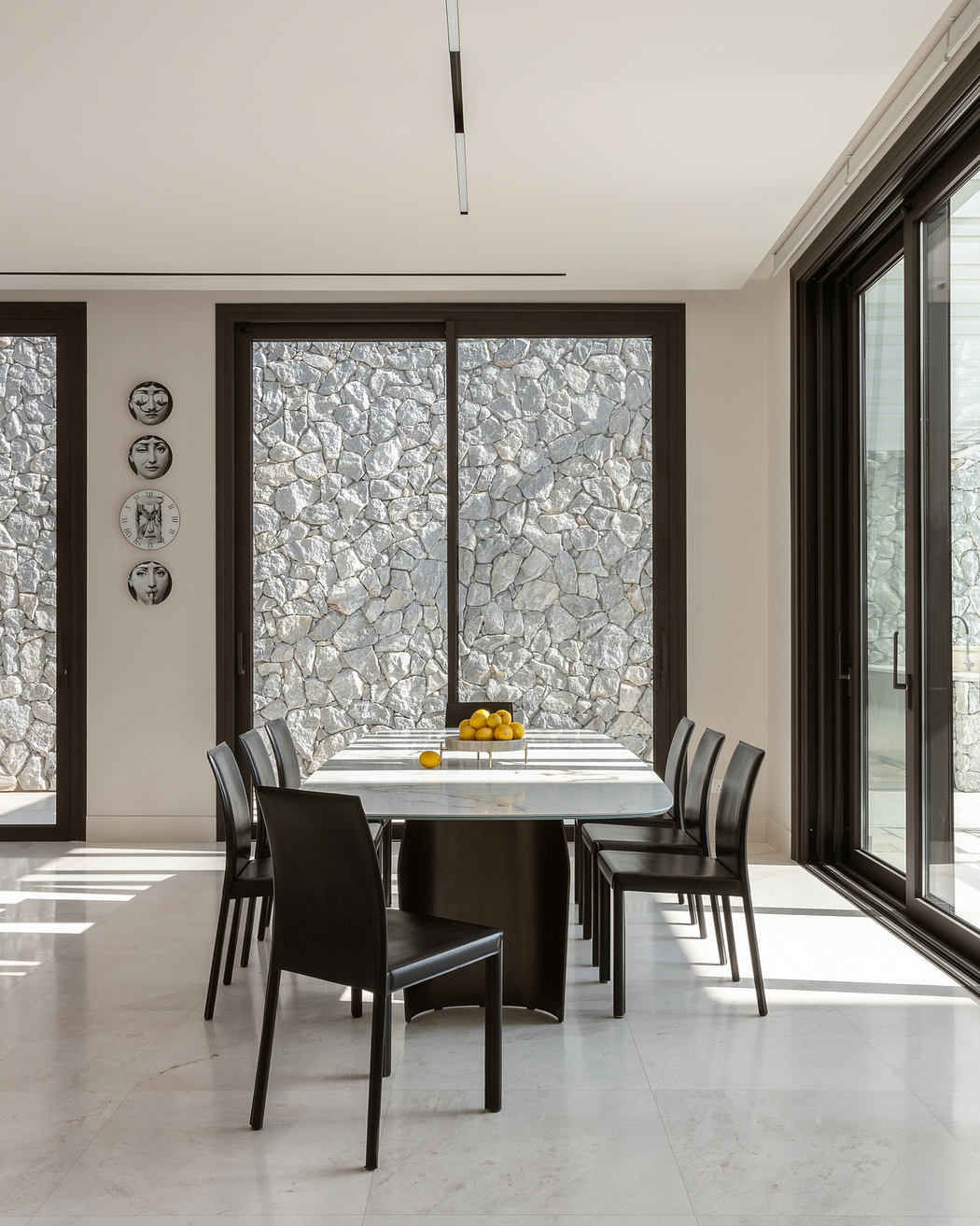 Modern dining room with stone walls, marble table, and black leather chairs.