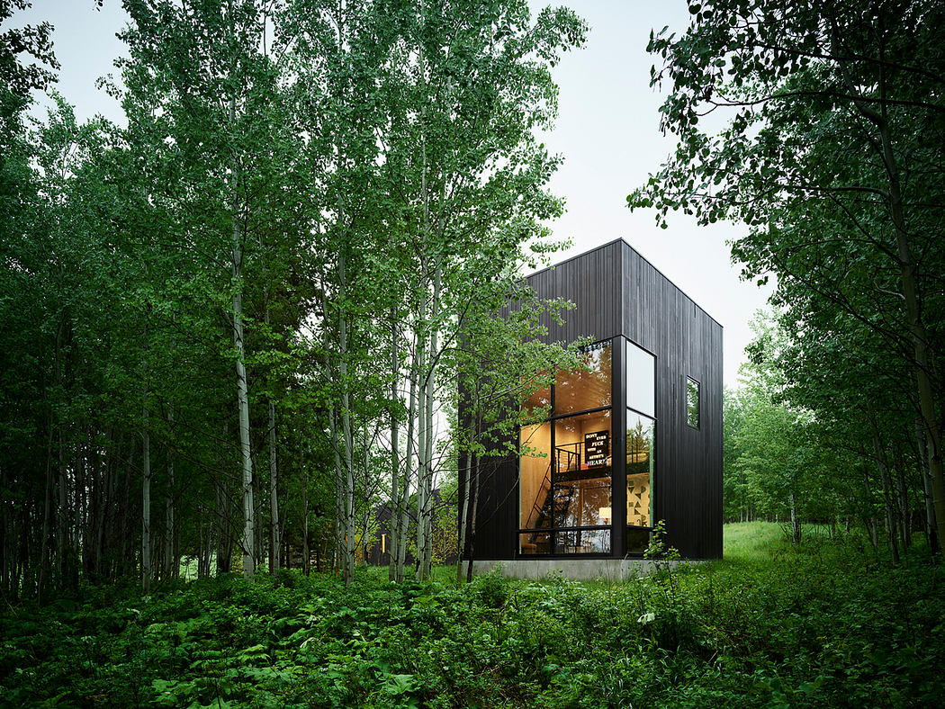 A modern dark wooden cabin nestled in a lush, green forest with large windows.