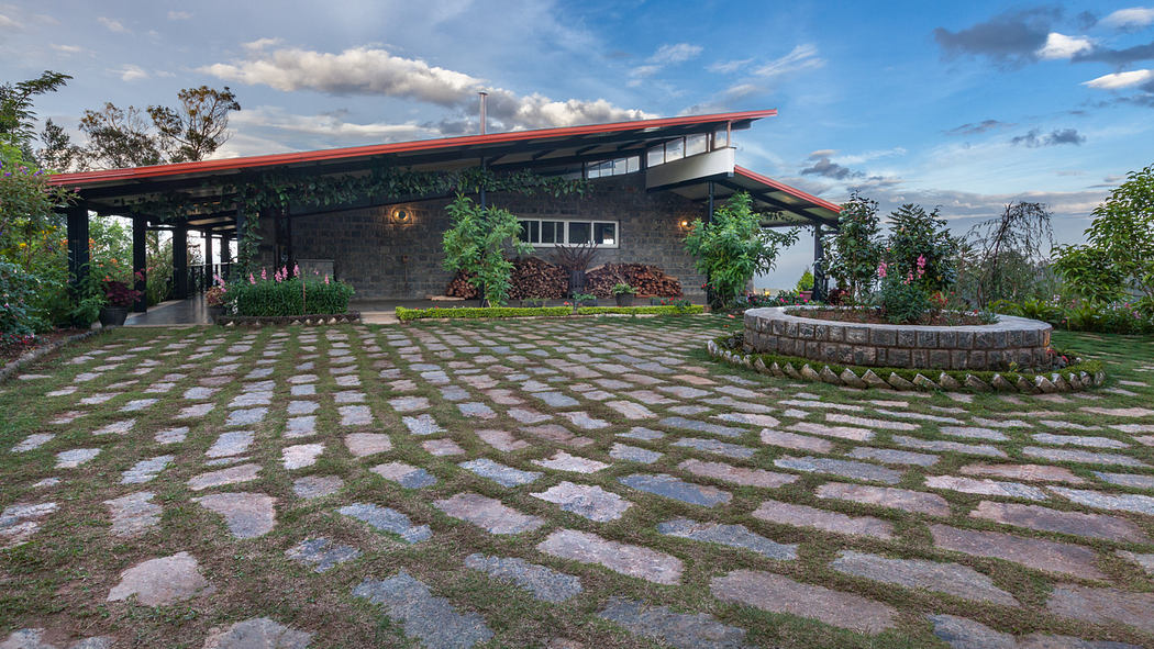 A modern, glass-paneled building with a red roof and a stone-paved courtyard surrounded by lush vegetation.