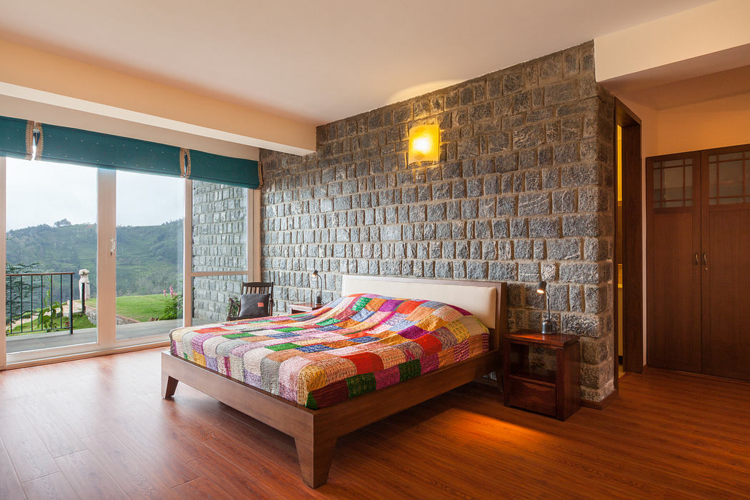 Cozy rustic bedroom with stone wall, wood floors, and vibrant patchwork quilt.