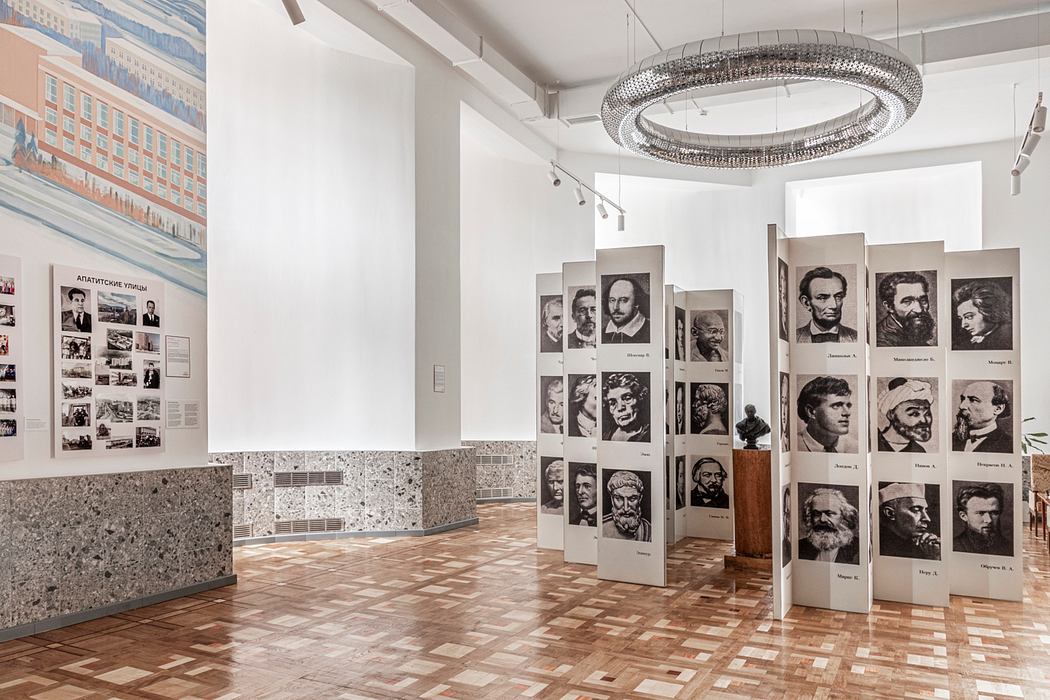 A spacious modern art gallery with a grand circular chandelier and artistic wall displays.