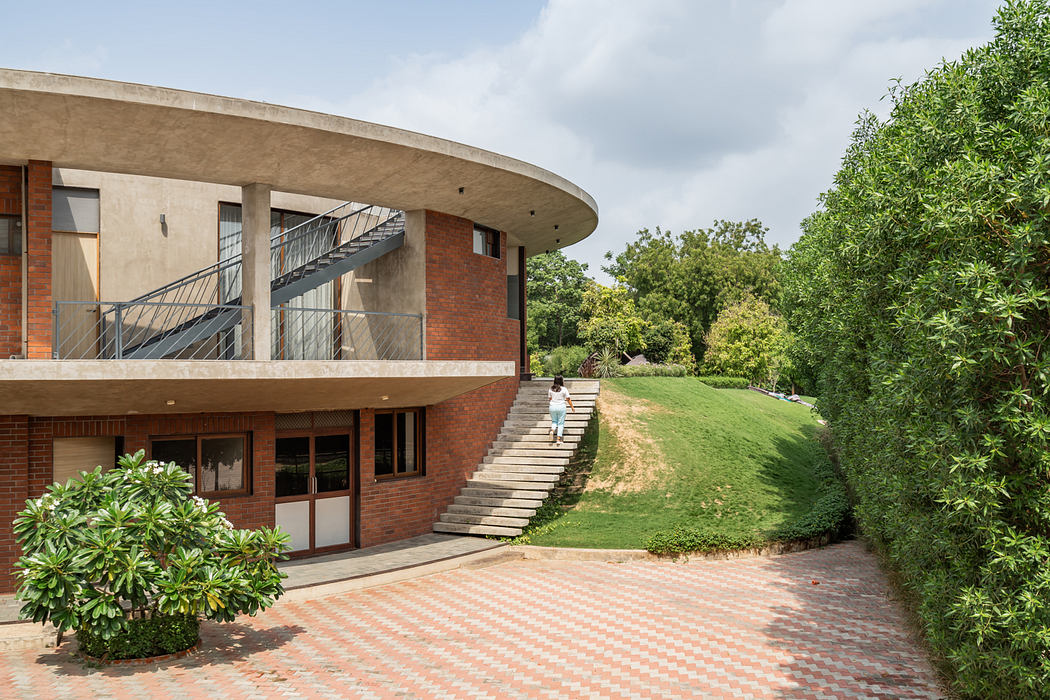 A curved, two-story brick building with a balcony, nestled in a lush, green landscape.