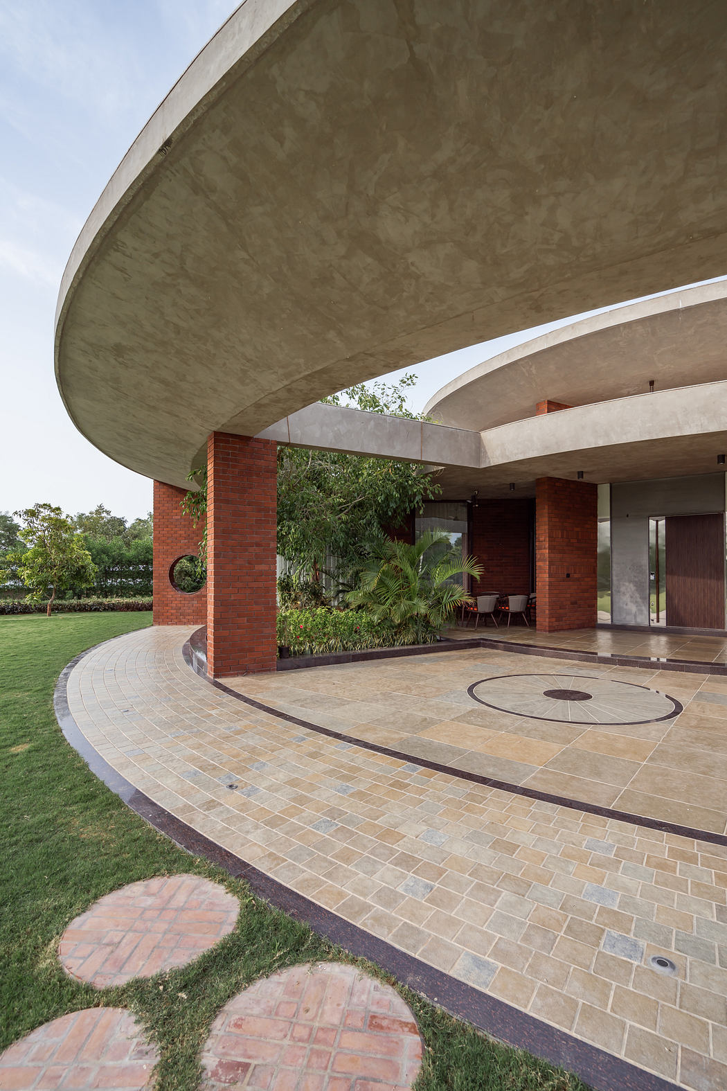 Modern architectural design featuring curved concrete canopy, brick columns, and tiled patio.