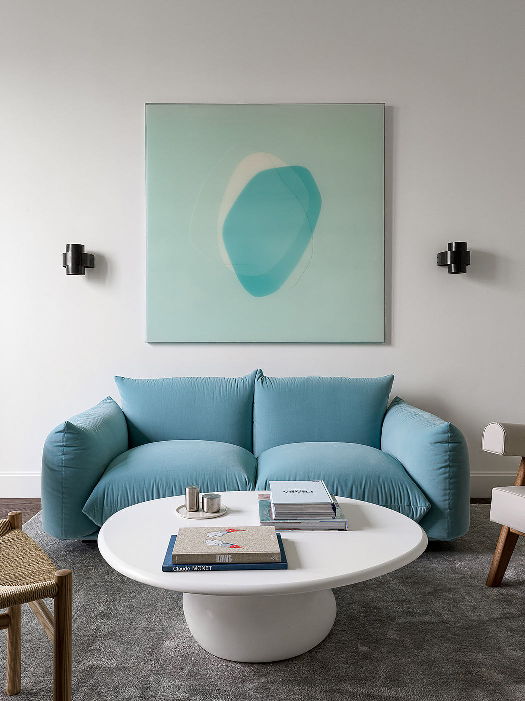 Clean, minimalist living room with turquoise sofa, white round coffee table, and modern artwork.