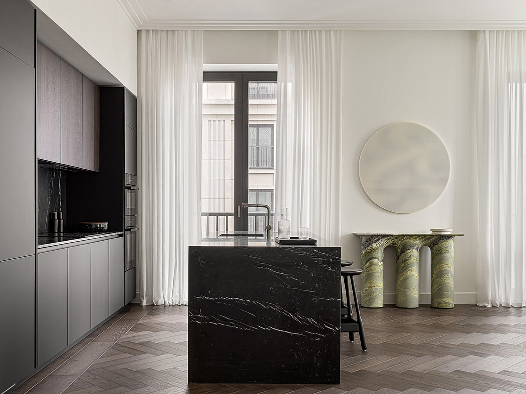 Sleek modern interior with black marble kitchen island, white curtains, and herringbone wood floors.