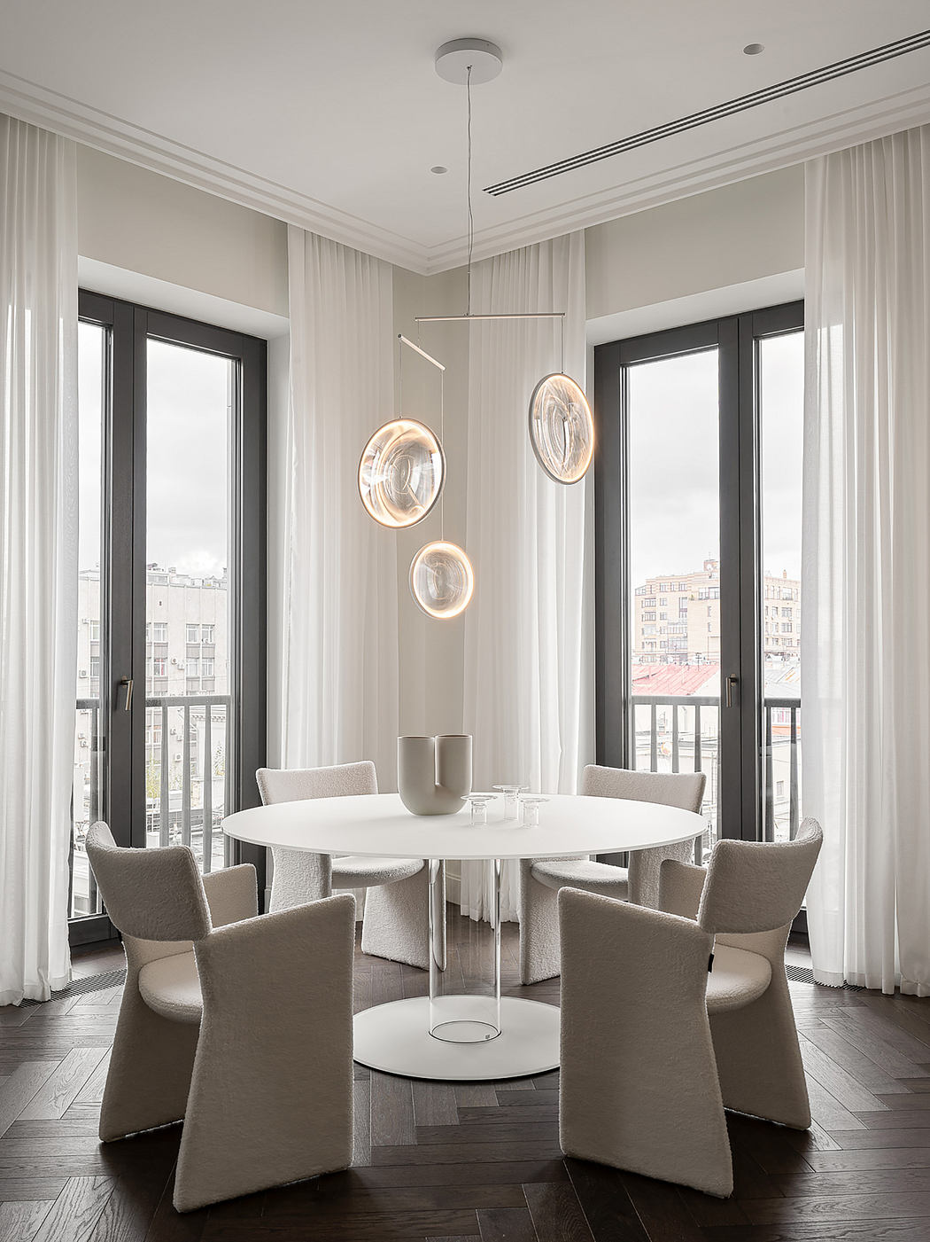Contemporary dining room with round table, pendant lighting, and large windows overlooking city.