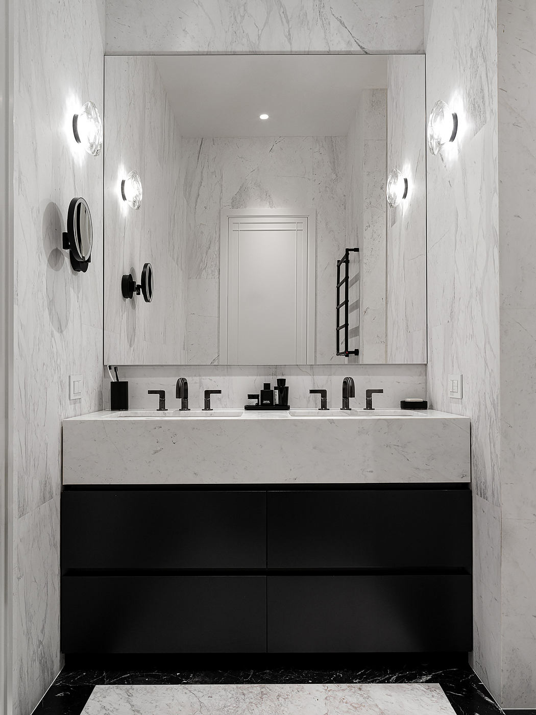 Sleek, monochromatic bathroom with marble walls, black vanity, and recessed lighting.