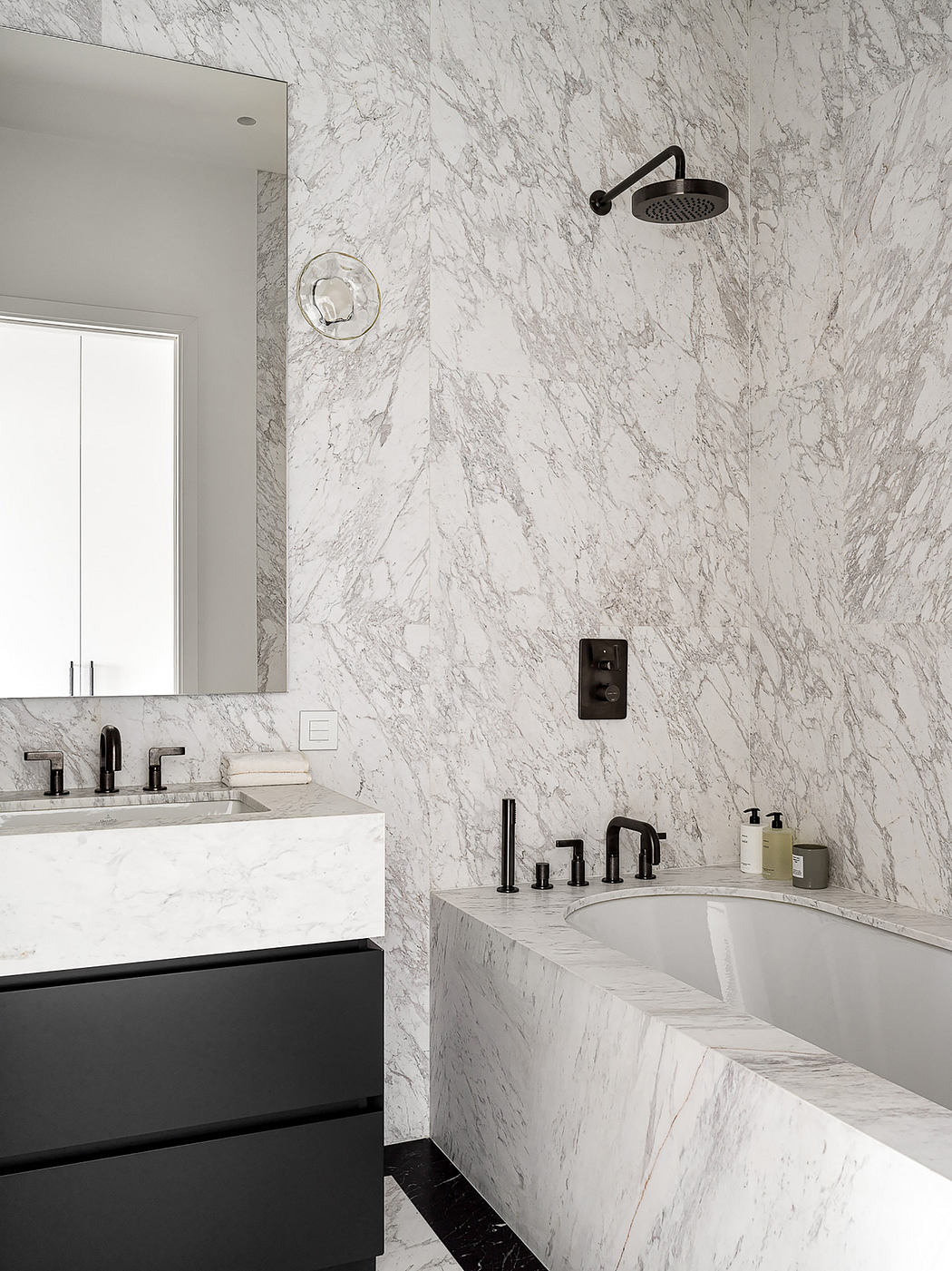 Modern bathroom with sleek black fixtures, white marble walls, and a seamless vanity.