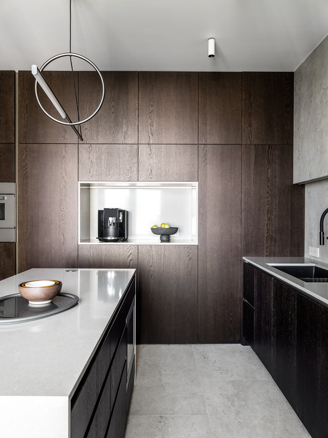Minimalist kitchen design with dark wood paneling, built-in appliances, and contemporary lighting.