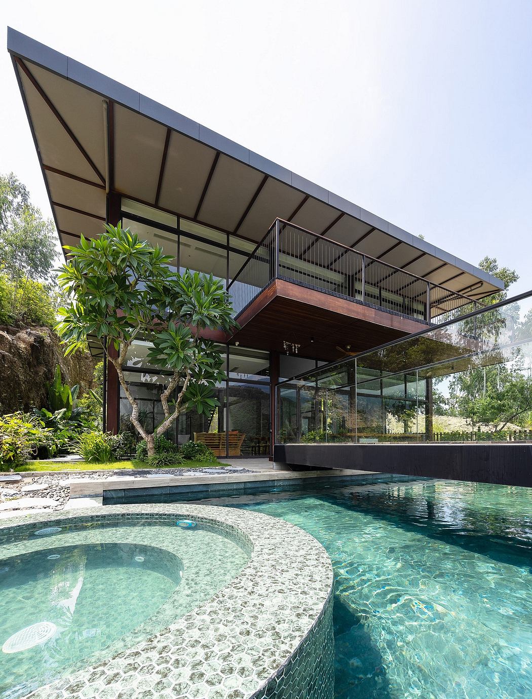 A modern, glass-walled home with a large pool, surrounded by lush greenery.