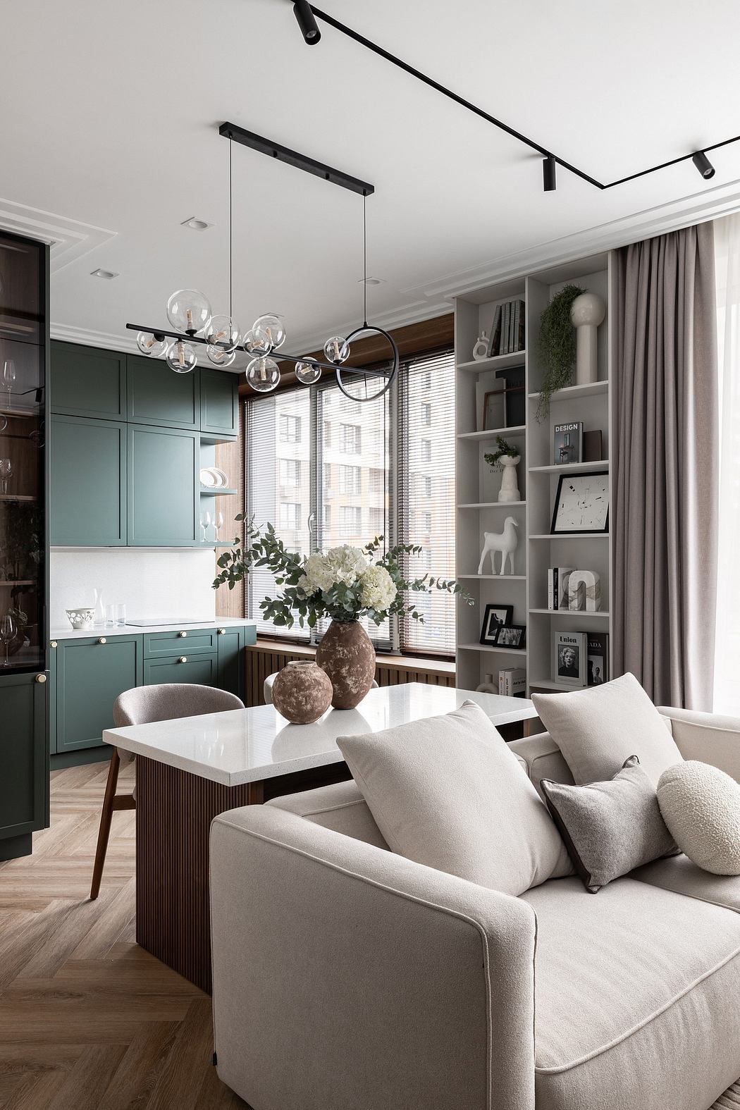 Spacious kitchen-living room with minimalist green cabinets, modern lighting, and cozy decor.