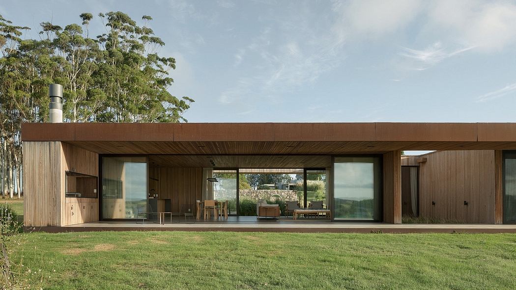 Modern wooden house with large windows overlooking a grassy lawn and lush trees.