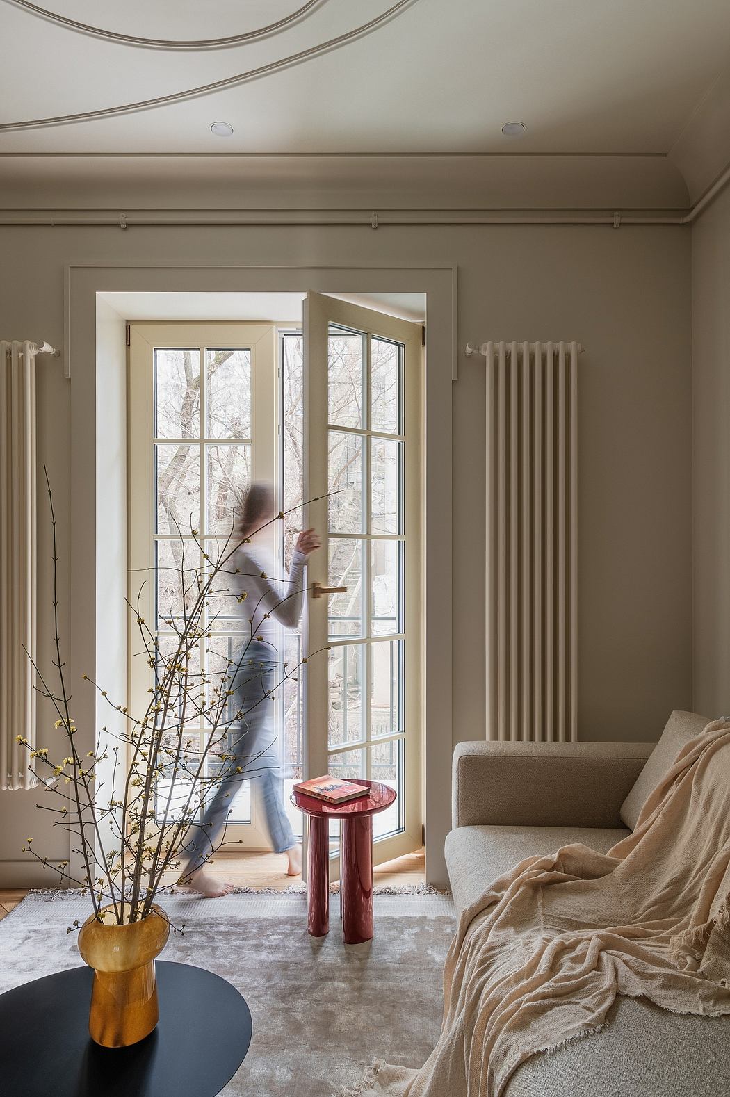 Cozy living room with large windows overlooking nature, warm beige tones, and a plush couch.