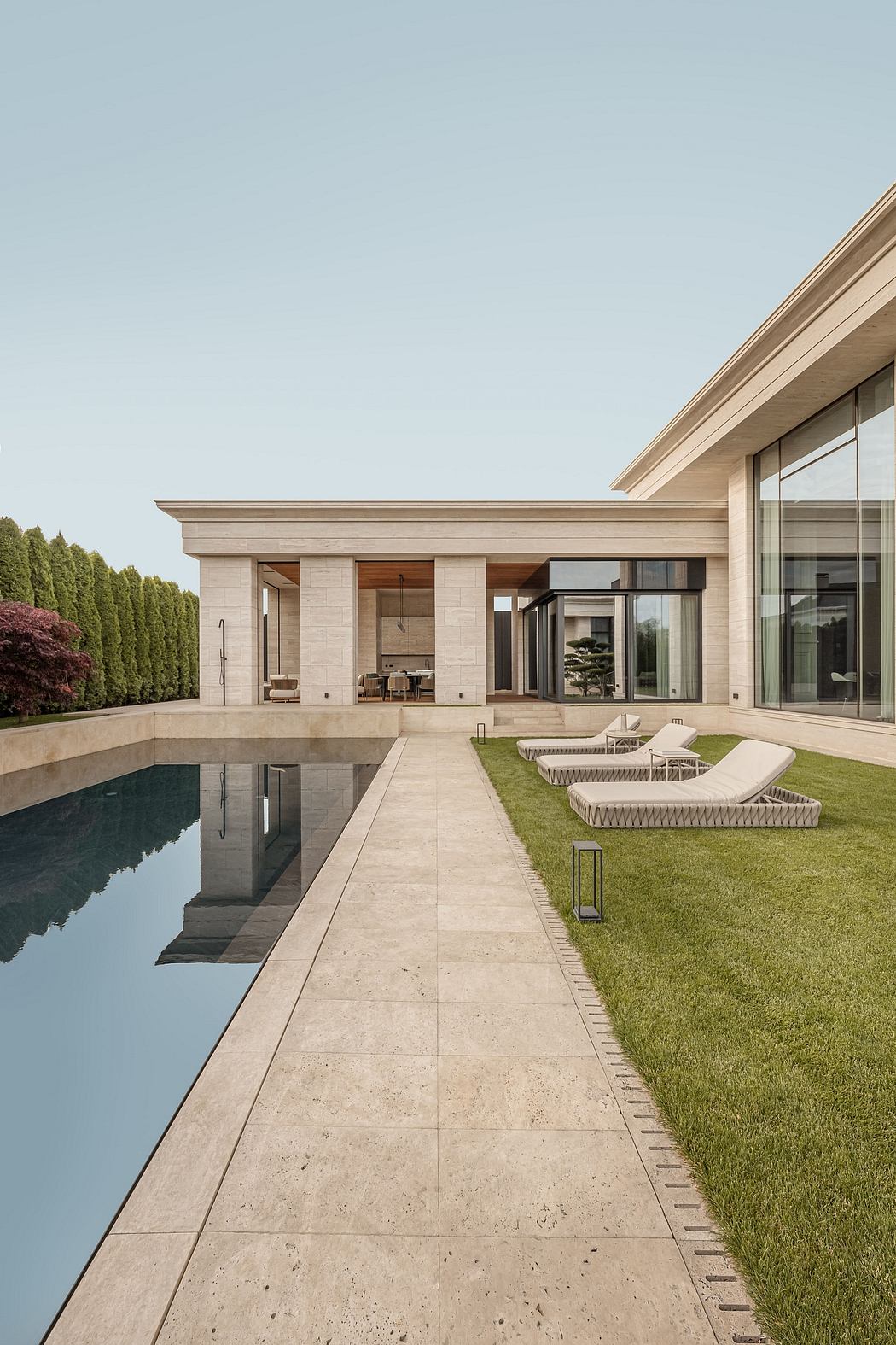 Sleek modern residence with stone exterior, glass walls, and pool reflecting the sky.
