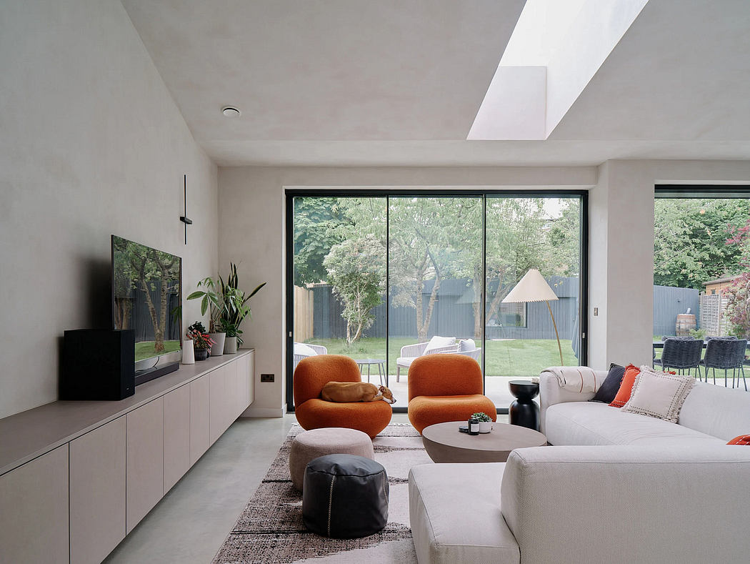 A modern, minimalist living room with floor-to-ceiling windows, plush furniture, and a lush outdoor view.