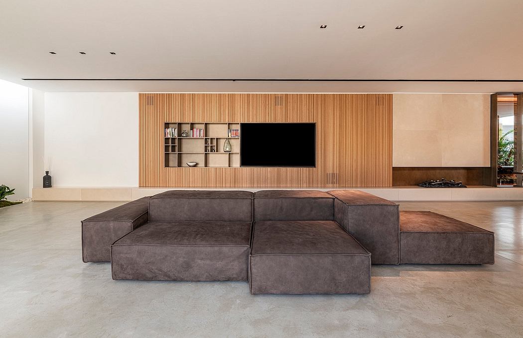 Sleek modern living room with a large gray modular sofa, built-in wooden shelving, and a TV wall panel.