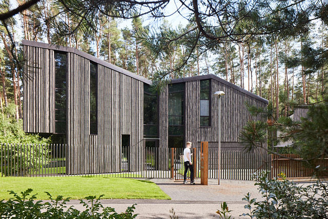 A modern, multi-story structure with vertical wooden slats and large windows nestled in a forested setting.