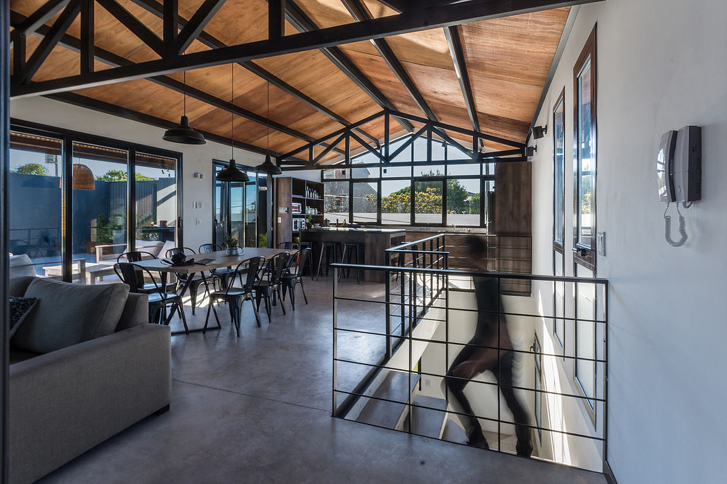 Open-concept industrial-style interior with exposed wooden beam ceiling, glass walls, and modern furniture.