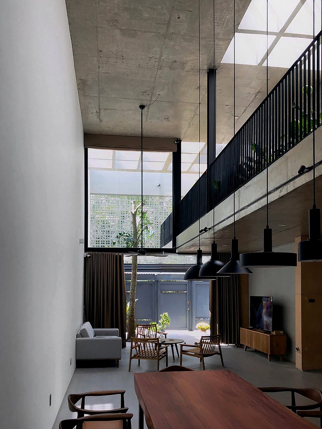 Concrete ceiling, black railings, large windows, wooden furniture, and lush indoor plants.