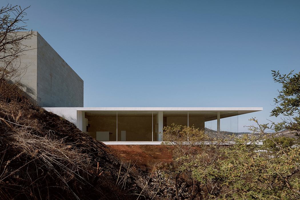 A modern concrete structure with a long cantilevered roof, surrounded by rugged terrain.