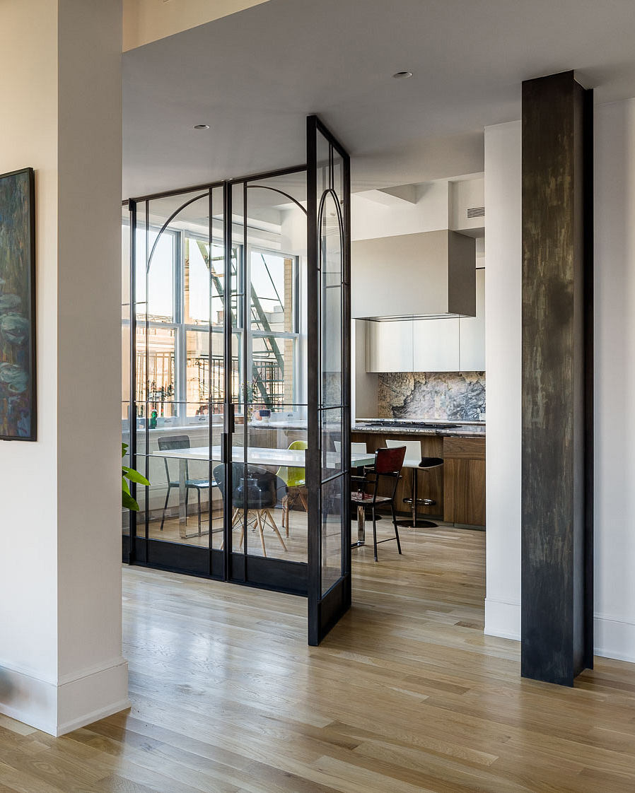 Modern open-plan kitchen with sleek glass partition, wood flooring, and industrial decor.