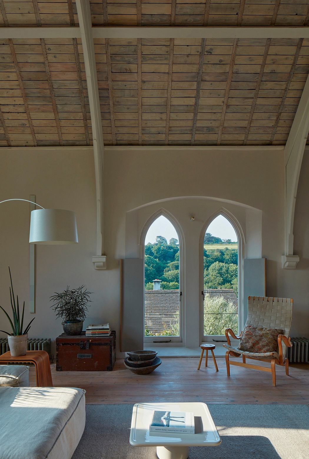 Rustic wooden beams, arched windows offer pastoral views, cozy furnishings.