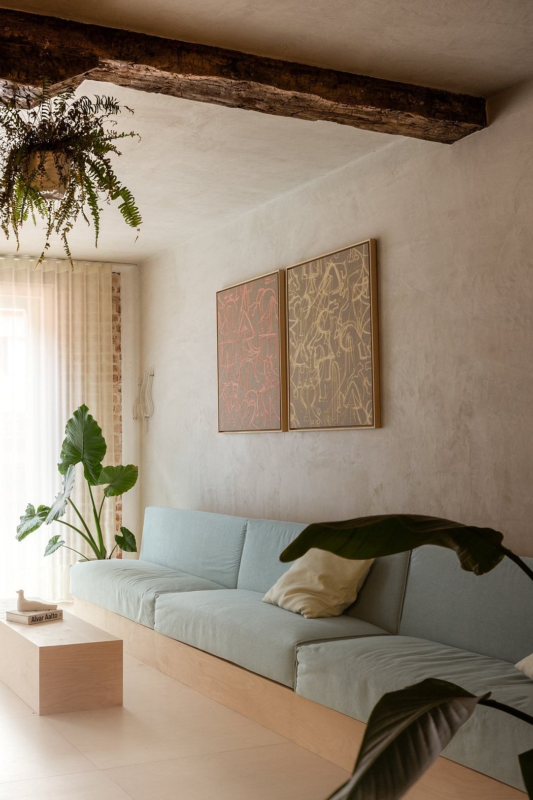 Cozy living room with exposed wooden beams, framed art, and lush greenery.