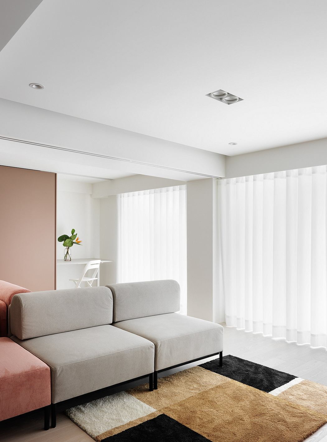 Minimalist living room with grey sofa, white curtains, and geometric area rug.