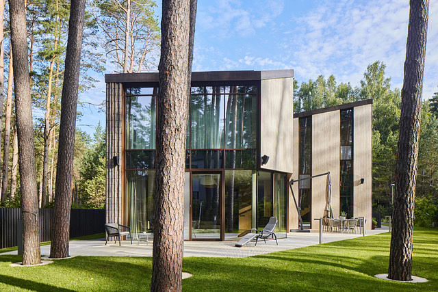 Modern glass and wood house nestled in a lush forest, featuring sleek architecture and an expansive outdoor terrace.
