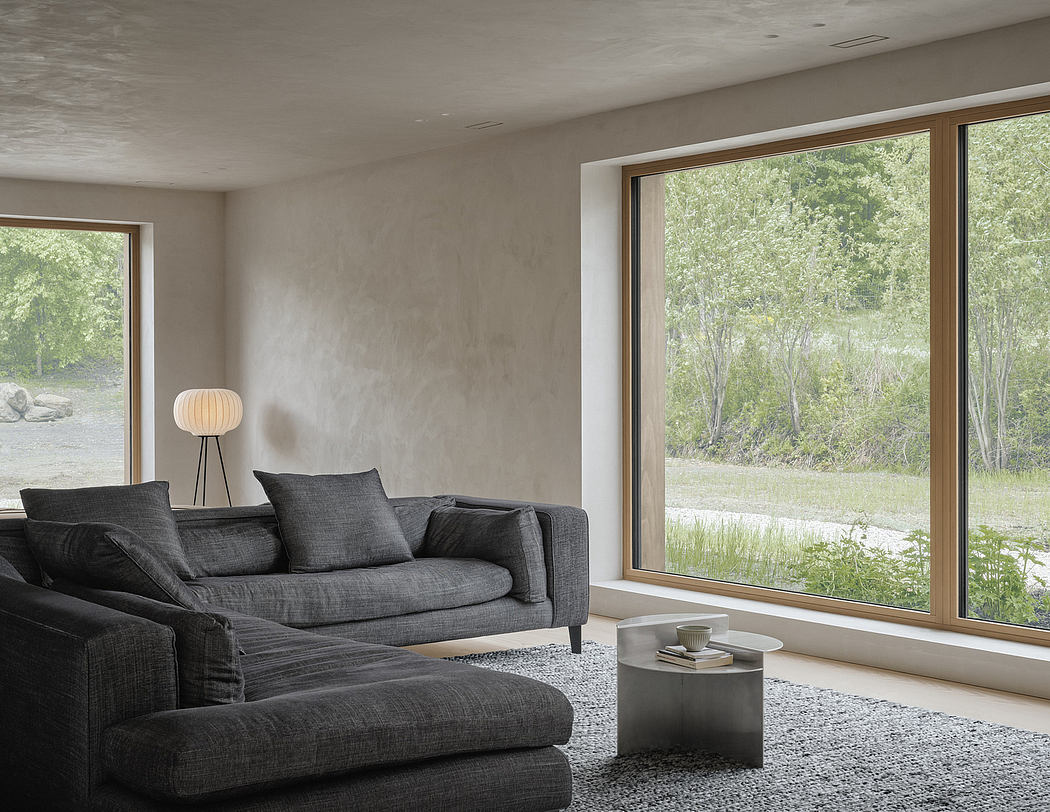 Modern living room with large windows overlooking lush green landscape, minimalist decor.