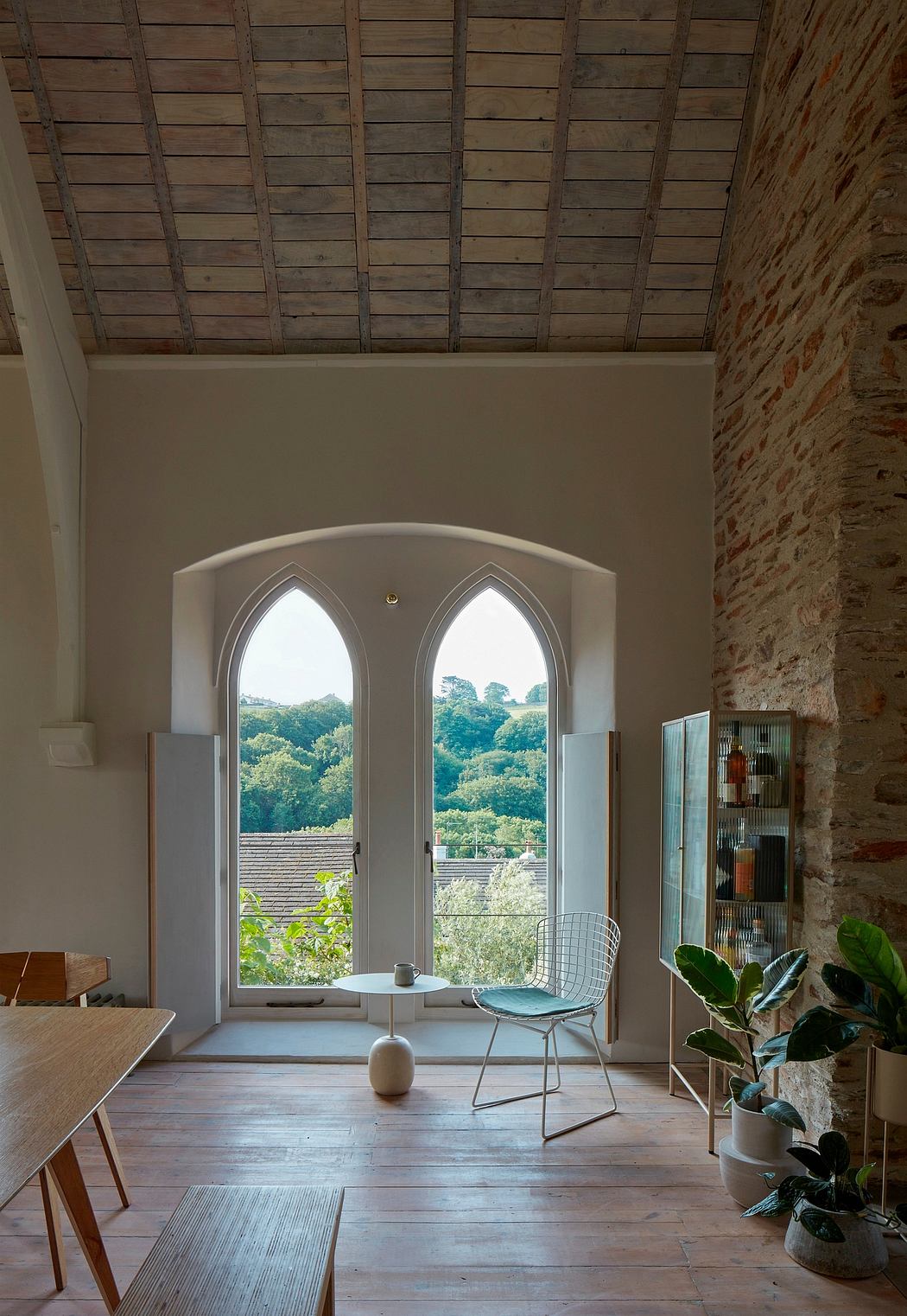 Arched windows frame a lush, verdant landscape in this cozy, rustic interior.