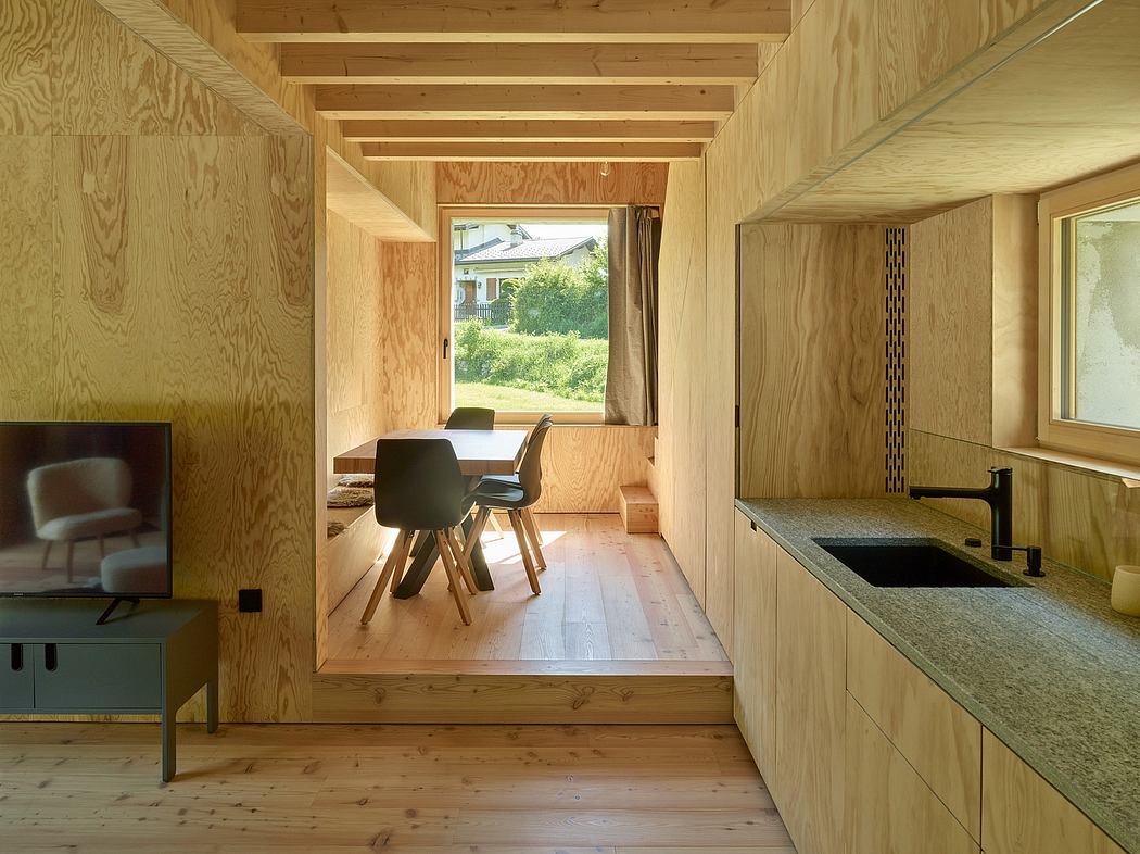 Warm wooden interior with minimalist furnishings, large window framing outdoor greenery.