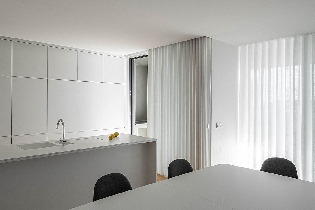 Minimalist kitchen with sleek gray cabinets, sink, and a dining table with black chairs.