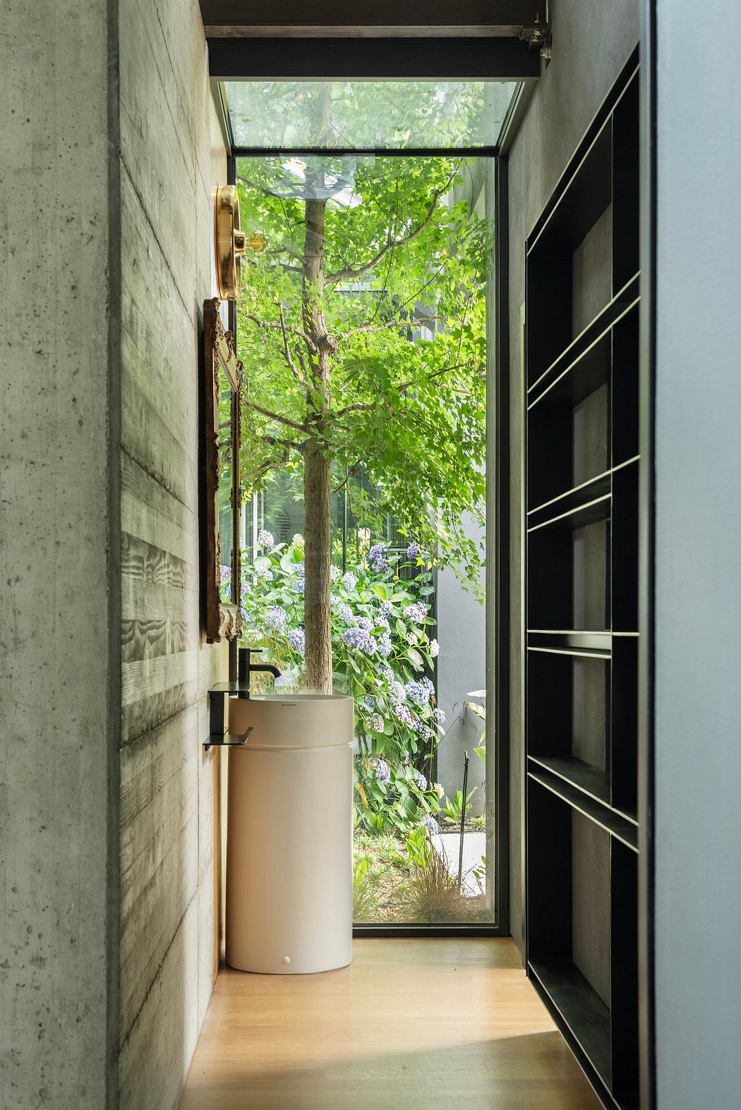 Compact hallway with concrete walls, glass doors, and lush greenery outside.