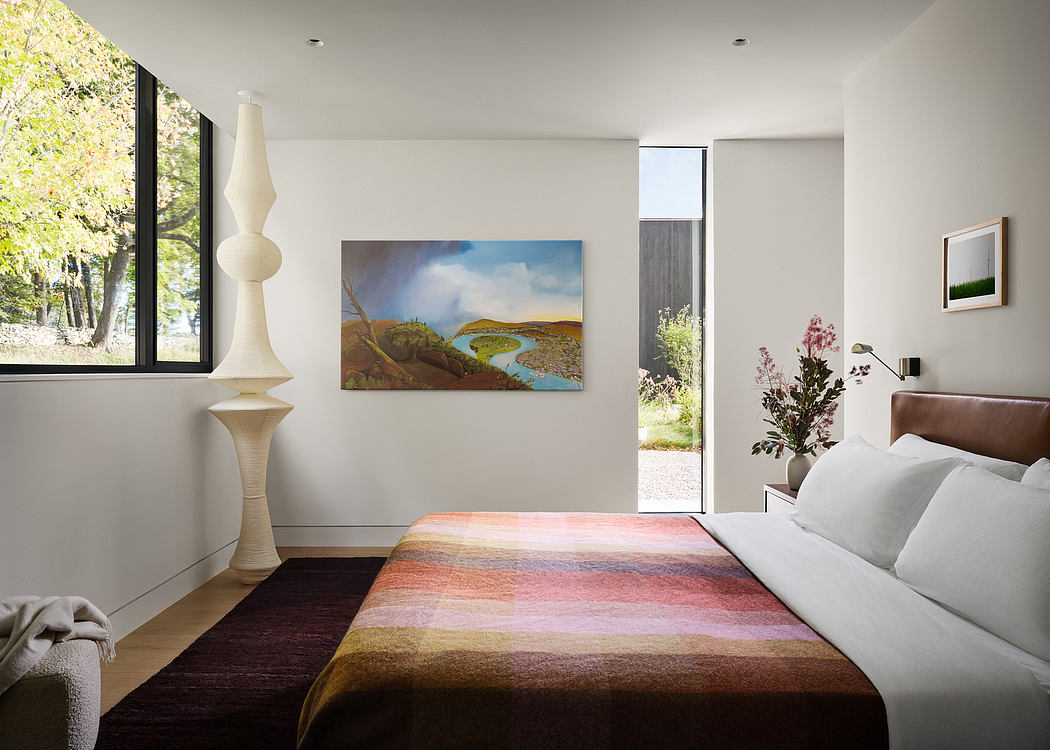 Minimalist bedroom with serene landscape artwork, modern lighting fixtures, and large window.