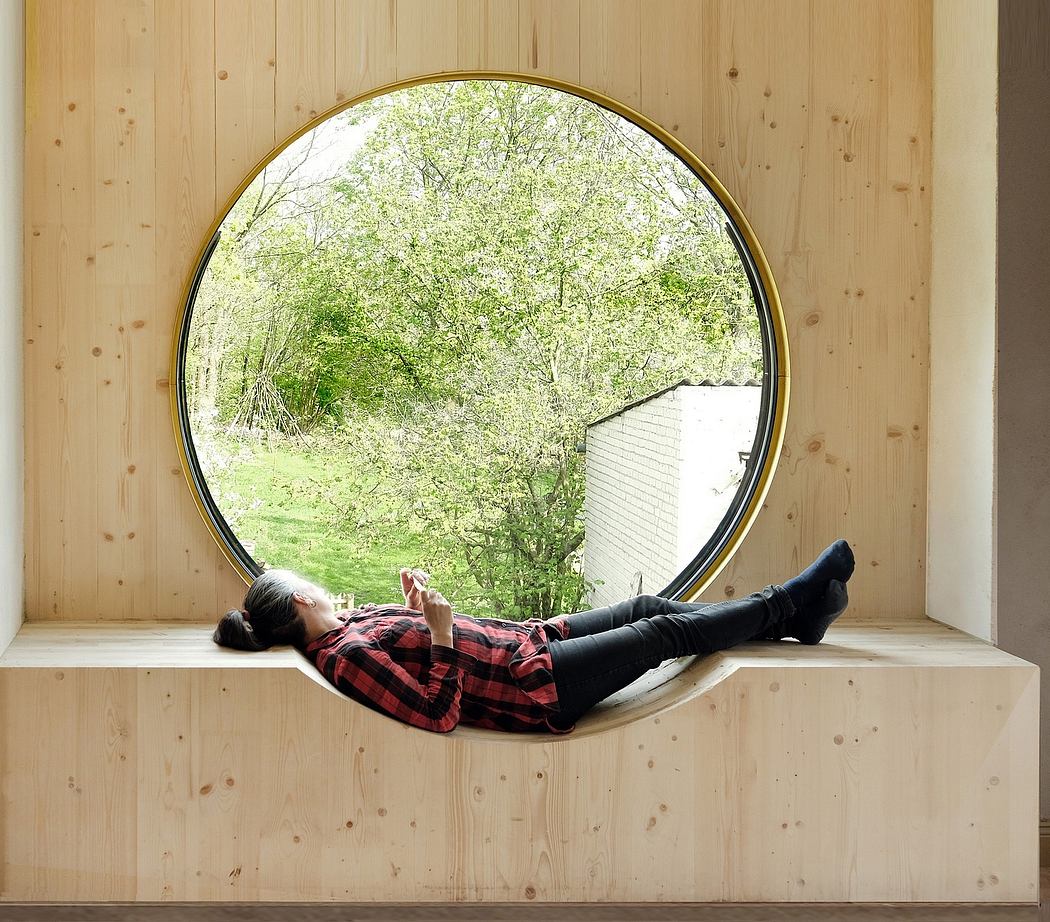 A circular wooden window frame provides a serene nature view from the cozy interior.