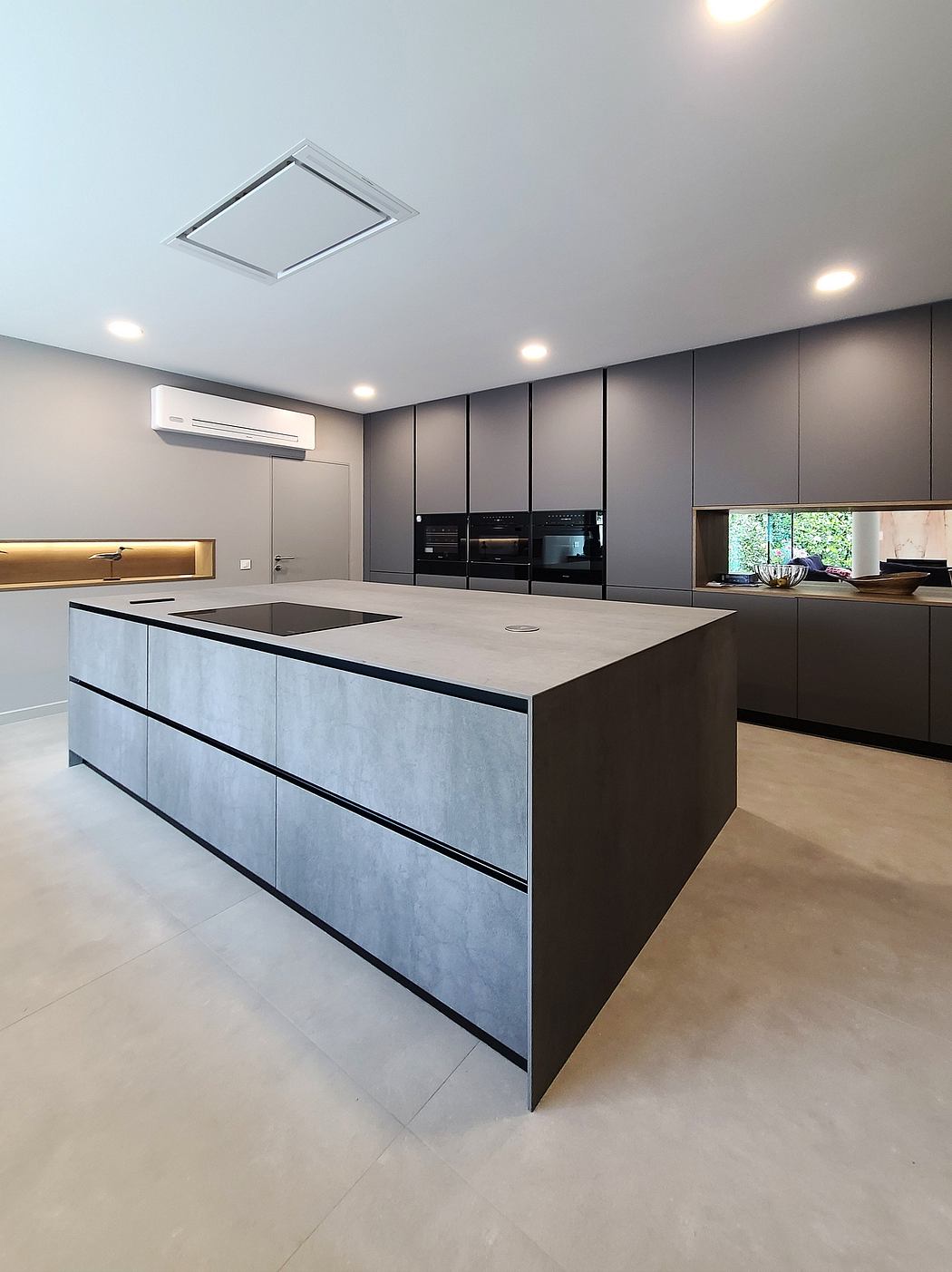 A modern kitchen with sleek, angular cabinets and a large central island with a concrete countertop.