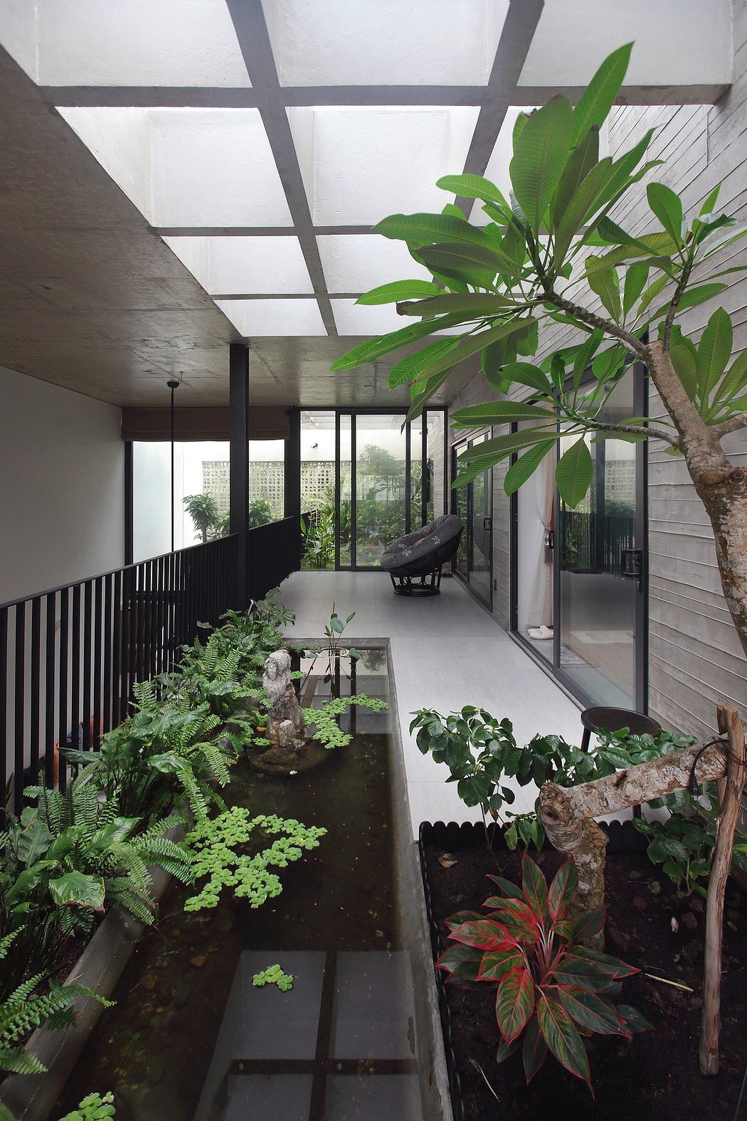 A lush, indoor garden with a modern, glass-walled architectural design, featuring various plants and an integrated water feature.