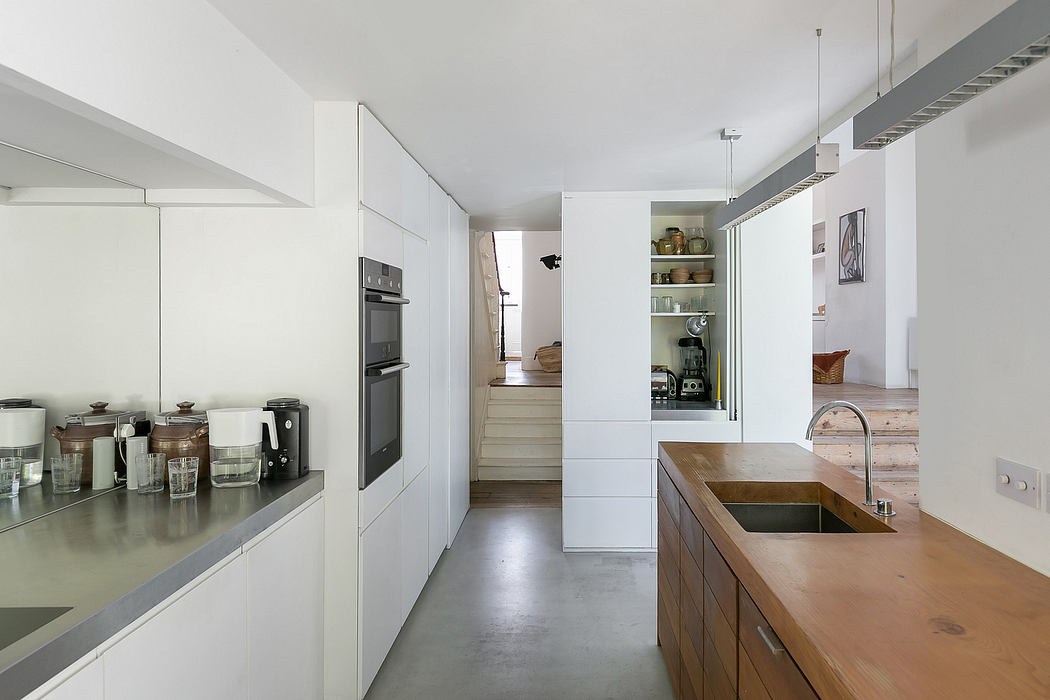 A modern kitchen with sleek white cabinetry, wooden countertops, and open shelving.