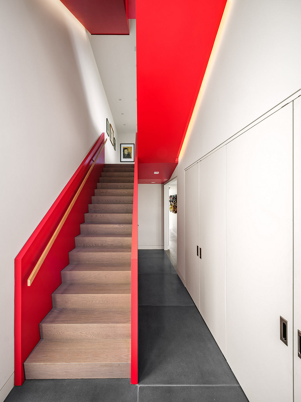 Striking modern staircase with wood treads and vibrant red walls, leading to upper floor.