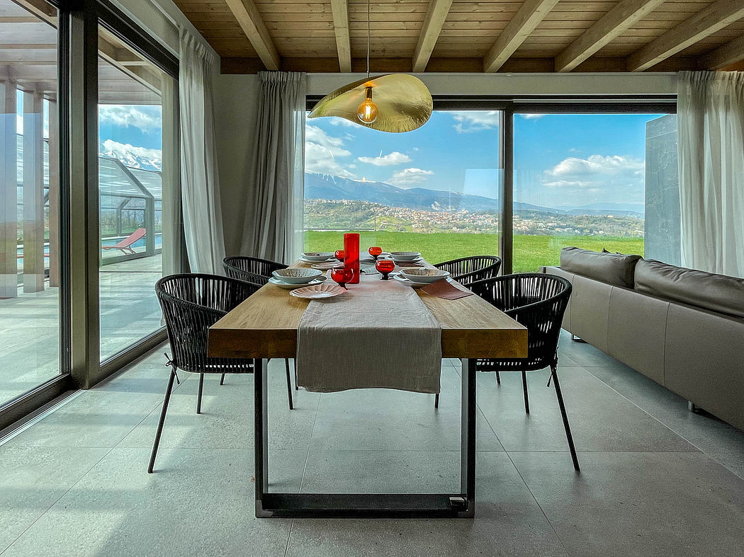 A spacious dining area with a modern wooden table, black wicker chairs, and a panoramic view of the surrounding landscape.