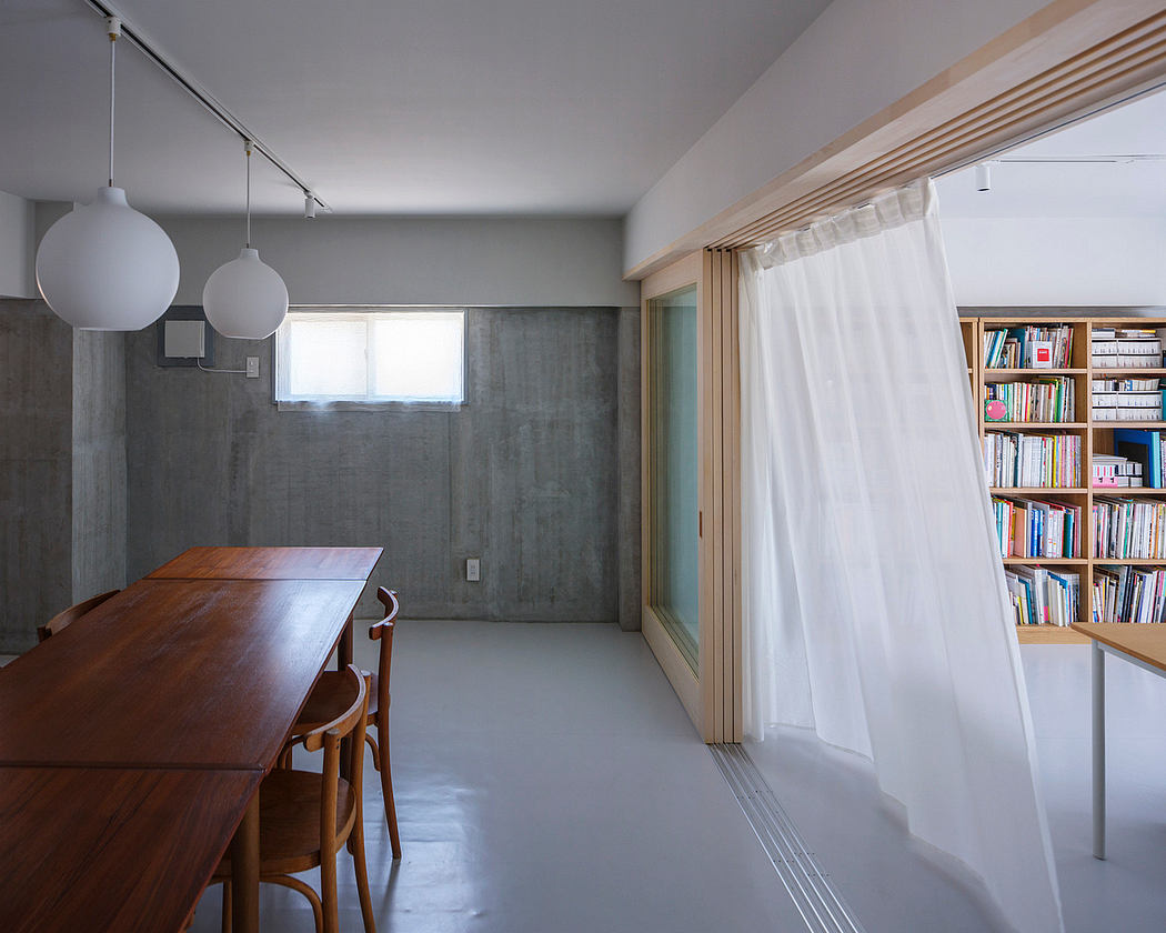 Minimalist open-concept space with concrete walls, wooden table, and built-in bookshelves.