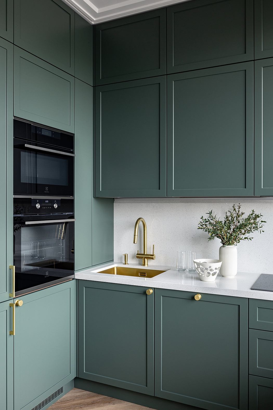 Modern kitchen with dark green cabinets, brass fixtures, and sleek white countertops.