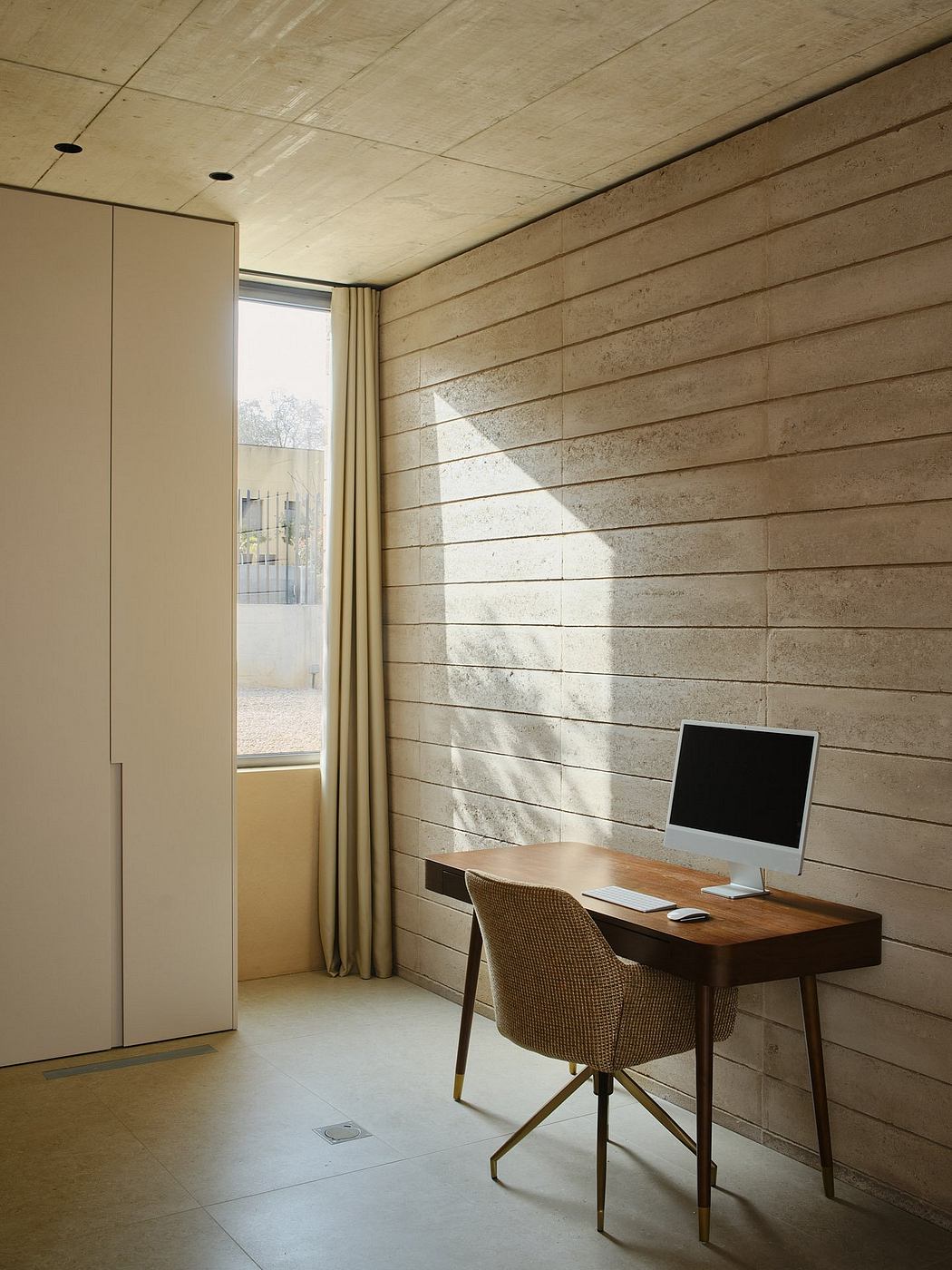 Minimalist home office with wooden desk, chair, and patterned concrete walls.