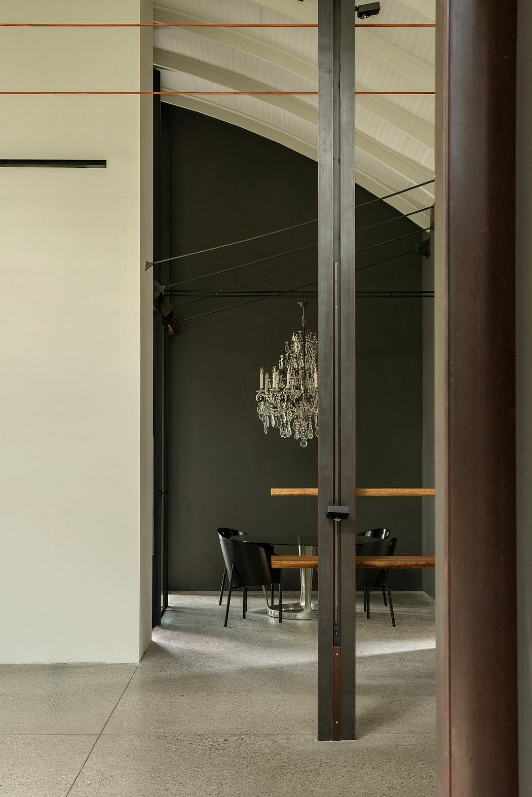 A minimalist interior with a large, ornate chandelier suspended above a table and chairs.