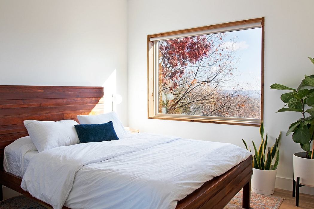 Cozy bedroom with wooden headboard, large window framing autumn foliage outside.
