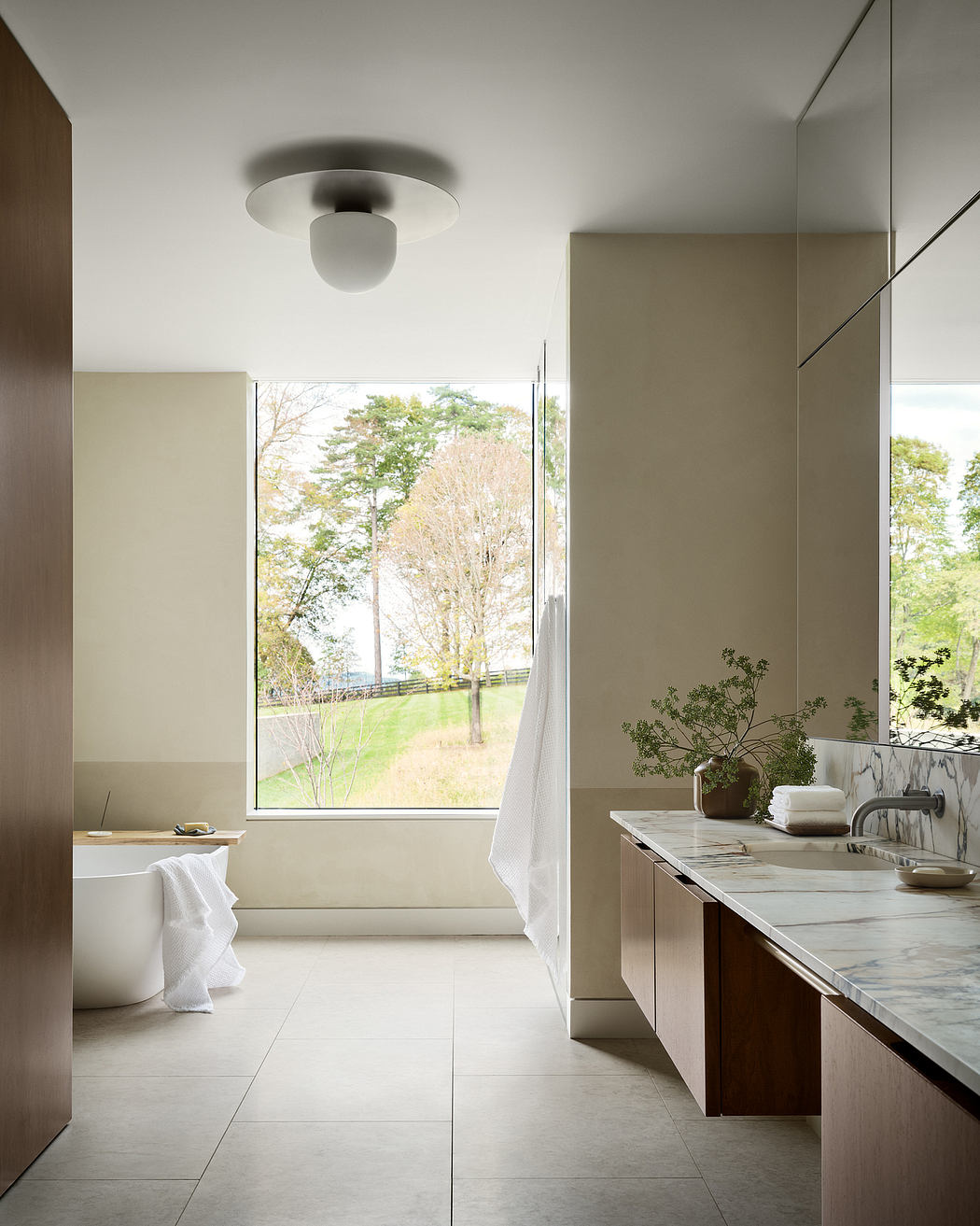 Minimalist bathroom with large window overlooking lush greenery outside. Sleek marble vanity and clean lines.