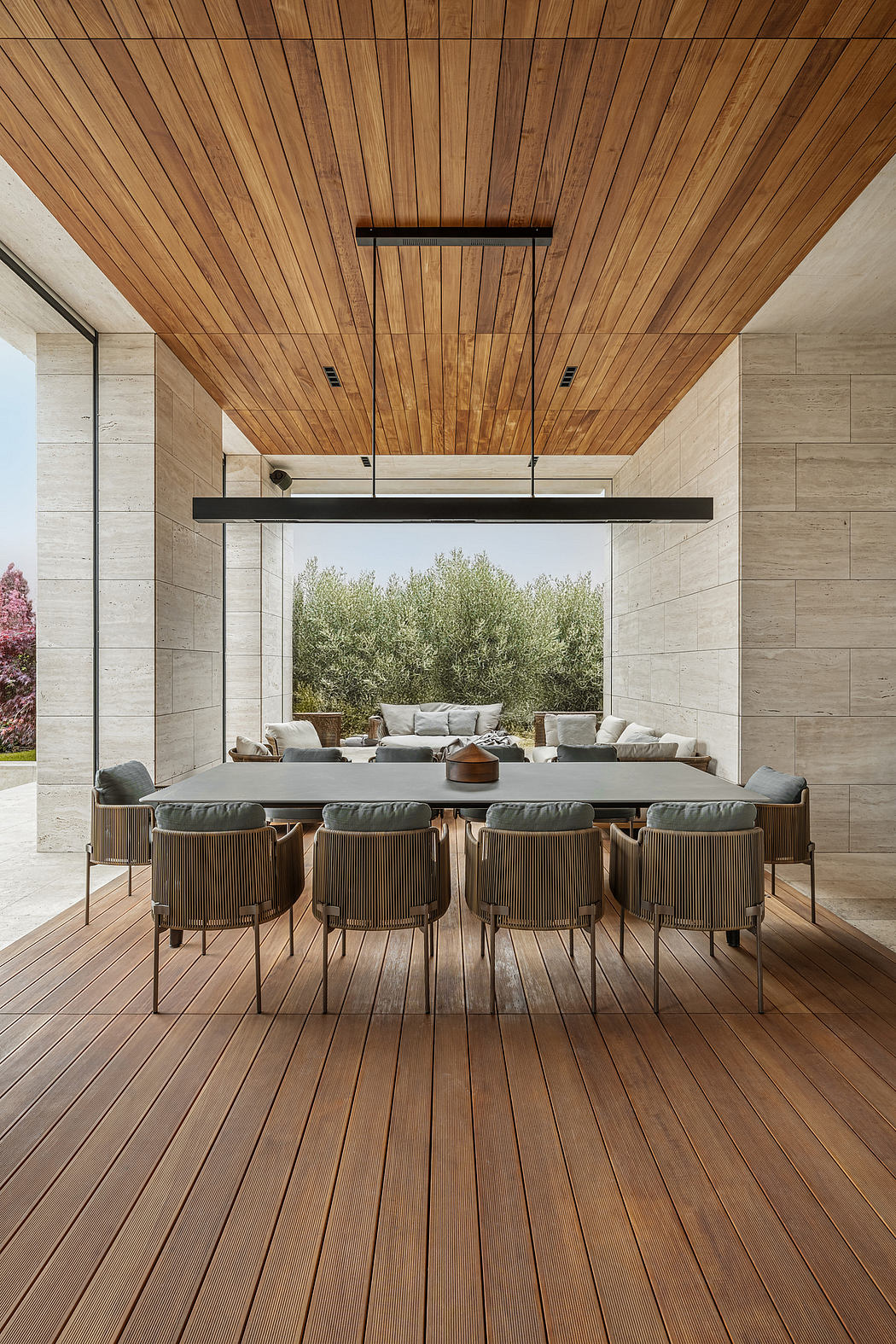 Expansive outdoor living space with modern wood-paneled ceiling, stone walls, and sleek dining set.