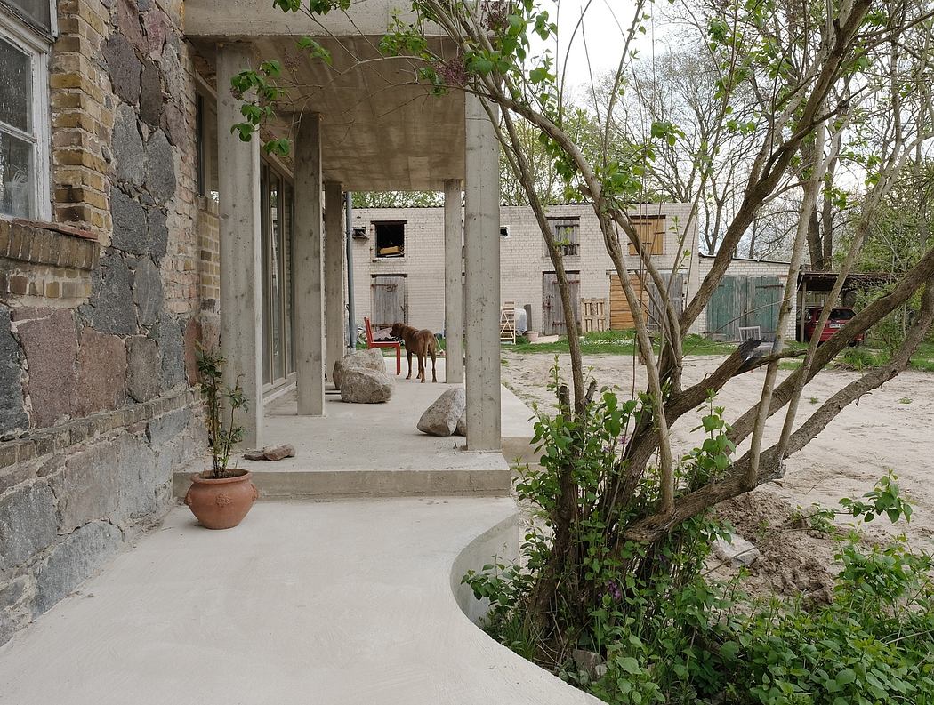 A weathered stone building with a covered walkway, surrounded by lush greenery.